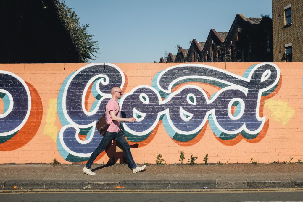 Person walking more each day through the city, behind him a wall has the word "good" written on